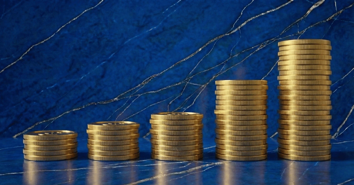 Five towers of golden coins stacking progressively higher, set against a deep blue marble background with golden veins, symbolizing the growth of wealth through investing.